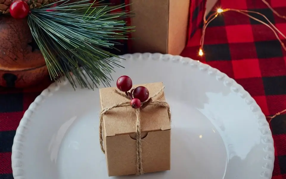 A small kraft gift box tied with twine and red berries, on a festive table